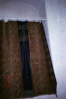 Close-up of a tallit, a Jewish prayer shawl, hanging from a rod. Deep blue with gold embroidery of Hebrew script and floral p...