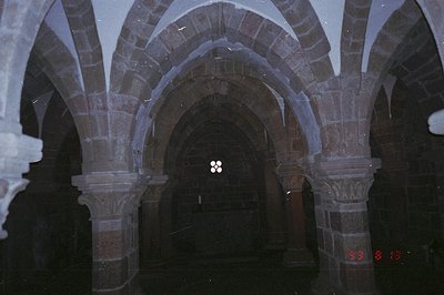 A view through a series of stone arches, showcasing a ribbed vault ceiling. Visible is a rose window at the end of the corrid...