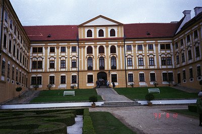 Elegant Baroque palace facade with symmetrical window arrangement and prominent central doorway. Formal courtyard garden with...