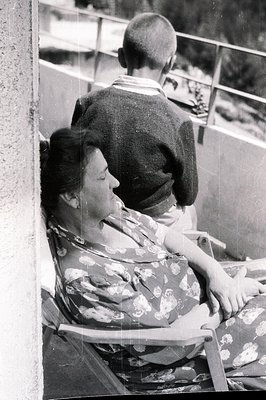 A woman in a floral-patterned dress rests on a metal folding chair, seated close to a man in a gray sweater. Likely a candid ...