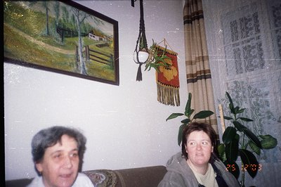 Two women sit on an ornate floral sofa, posed for a photo likely taken in the 1970s or 80s. A landscape painting hangs on the...