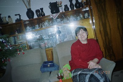 A seated person in a red sweatshirt and patterned trousers smiles for the camera. A decorated Christmas tree is visible to th...