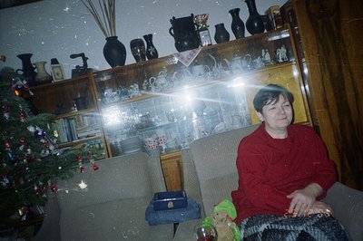 A man sits on a patterned armchair in a room decorated for Christmas. A fully decorated tree stands to the left. The room's u...