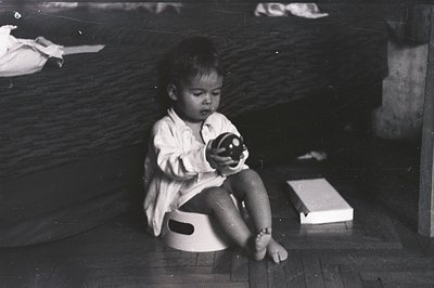 A young child, seated on a training toilet, holds a small, round object, likely a toy. The scene appears domestic, with a tex...