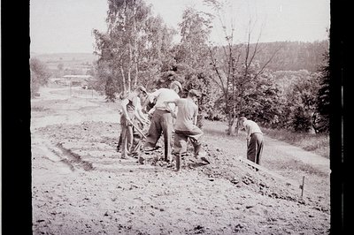 Group of men laboring on an earthen embankment, possibly road construction. Visible tools include shovels & what appears to b...