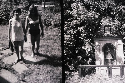 Two young women walk barefoot on a gravel path, one in a floral dress, the other in a dark one-piece swimsuit. Lush foliage f...