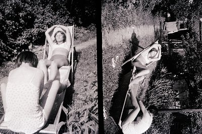 A young woman reclines in a wooden deck chair amidst overgrown greenery. Shot appears to be from the 1970s, judging by clothi...