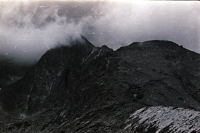 Dramatic, grayscale landscape features a rocky mountain peak shrouded in swirling mist. Textured slopes, appearing sparsely v...