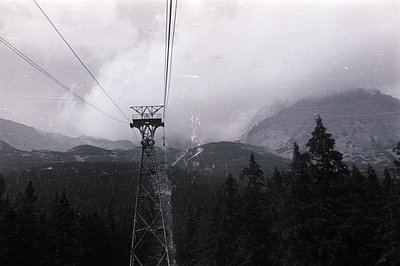 Dramatic monochrome view of a ski lift tower set against a backdrop of snow-capped mountains partially obscured by low-hangin...