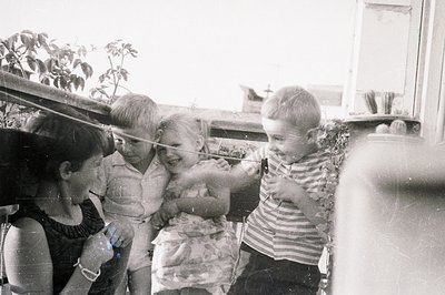 Four children clustered on a balcony, seemingly engaged in a game. The scene appears domestic, with glimpses of surrounding b...