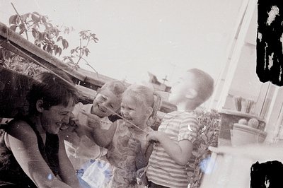 A candid snapshot depicts three children and an adult on what appears to be a seaside terrace. The children are playfully int...