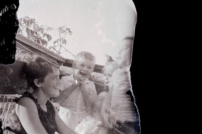 A candid, black and white photo captures three children outdoors, seemingly mid-laughter. The group appears to be on a patio ...