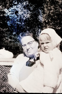 Man holds a young child with short blonde hair, likely a toddler, wearing a white bonnet. Both appear to be outdoors, amidst ...