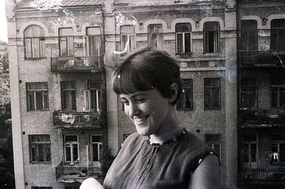 Young woman with a stylish bob, smiling directly at the camera. She wears a dark, tailored dress with a high collar. The back...