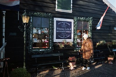 A storefront in Amsterdam features Delft Blue pottery, jewelry, and watches. A person in a brown coat stands near, observing ...