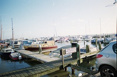 A vibrant marina scene featuring numerous sailboats and motorboats moored in calm water. A weathered wooden pier and signage ...