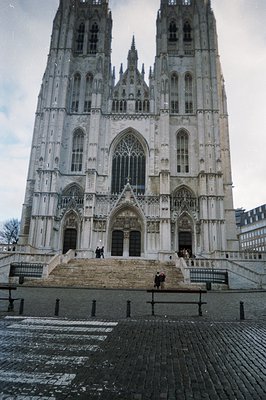 Grand, imposing Gothic cathedral façade featuring intricate stonework, pointed arches, and soaring spires. People ascend the ...