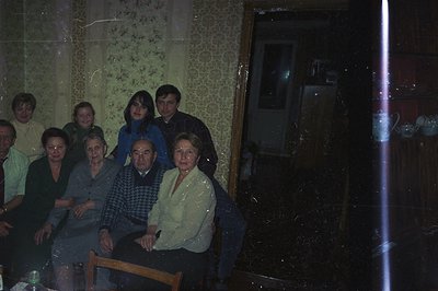 A multigenerational family group poses indoors. A formal, posed portrait with elderly relatives seated and younger members st...