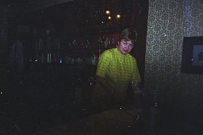 A man in a bright yellow short-sleeved shirt appears to be bending over something unseen, set against a wall with distinctive...