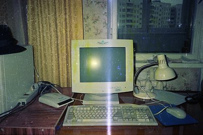 A beige, CRT computer monitor displays a bright, central spot of light. A keyboard and mouse sit on the desk. A lamp and exte...