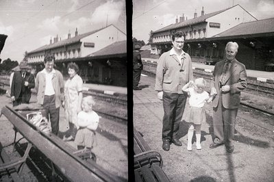 <start_of_image> This monochrome photograph captures a family portrait at a railway station platform. A man, woman, and young...