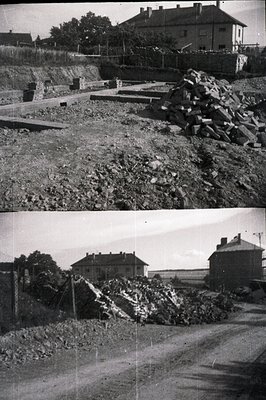 B&W image of demolition site. Rubble piles flank a narrow road leading towards a row of brick homes. Likely post-war reconstr...