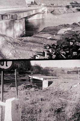 Monochrome photo captures bridge construction over a river. Visible concrete structures & pile of rocks suggest ongoing work....