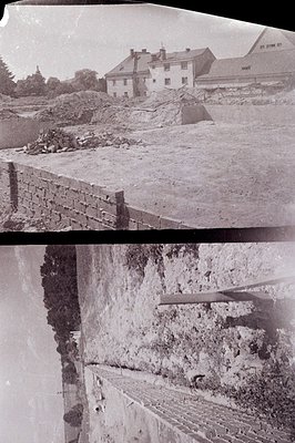 An exterior view of a brick retaining wall under construction, likely part of a larger landscape project. A large, multi-stor...