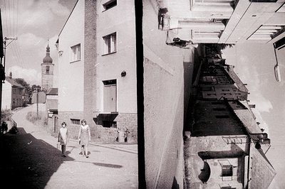 A young girl walks along a cobblestone street lined with early 20th-century European architecture, possibly Central or Easter...