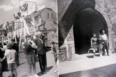 A monochrome view of a group gathered near a stone archway. Several figures, including men in suits and children in dresses, ...