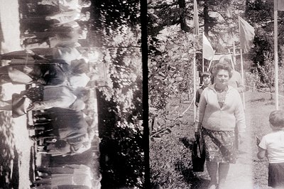 A candid black-and-white photograph shows a woman with a child in what appears to be a public park setting. The woman is hold...