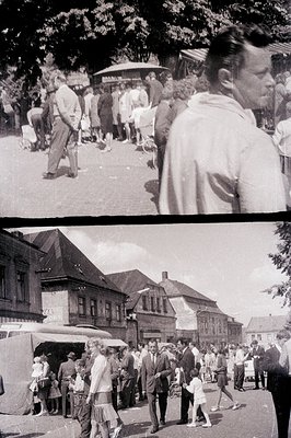 A candid black and white photograph capturing a bustling town square scene, likely in Eastern Europe. Multiple figures are pr...