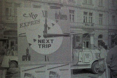 A monochrome image of a vintage bus displayed in a shop window, with a promotional poster for “Next Trip” and "Express" visib...