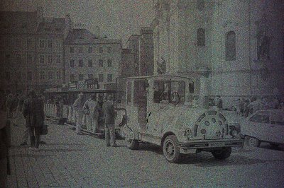 Black and white photo depicts a crowded street scene with a vintage bus and multiple pedestrians. Architectural background fe...