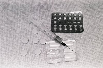 Close-up of a 5ml syringe and blister pack of pills on a textured surface. Several loose tablets lie nearby. Likely a represe...