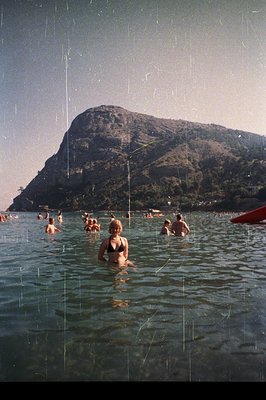 Group of bathers enjoy the turquoise waters of a seaside location, likely Bulgaria’s Varna, with a prominent, tree-covered cl...