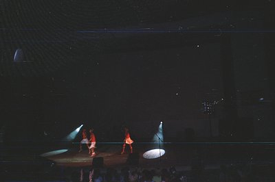 Stage performance captures dancers in dynamic poses, illuminated by spotlights. The dark backdrop and audience suggest a conc...