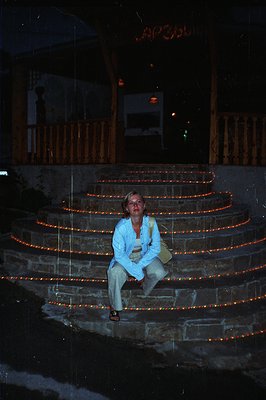 A woman sits on a staircase illuminated by numerous strings of small red lights. The architectural style suggests a resort or...