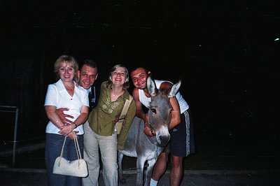 Group portrait featuring a family posing with a donkey at night. The subjects wear casual 1970s/80s attire - the woman carrie...