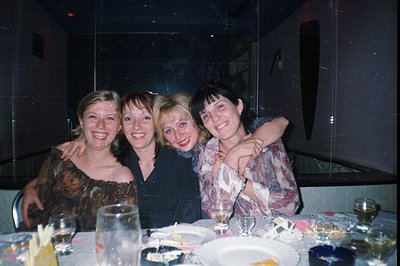 Four women pose closely during a festive dinner setting. The image, captured on film, displays a casual, intimate atmosphere....