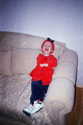 A young child, likely toddler-aged, sits on a large, shaggy, beige sectional sofa. They are wearing a red, furry hat with a b...