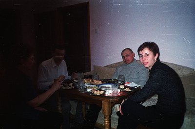 A family gathered around a dining table laden with food and drink, indicative of a celebratory or shared meal. The room appea...