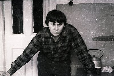 Striking black and white portrait of a young man with short, dark hair and intense gaze. He wears a plaid shirt, positioned n...