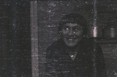 A vintage black and white portrait shows a man with a wide, unsettling smile looking directly at the camera through a scratch...