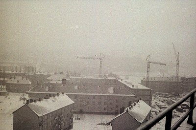 Overlooking a snow-covered cityscape. Dense snowfall obscures details, but residential buildings and industrial cranes are vi...
