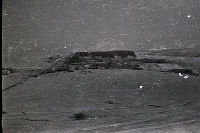 A monochrome landscape view shows a structure atop a low, rolling hill. Possible ruins or outbuildings are visible, with a we...