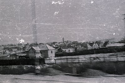 A grainy, black and white photograph showing a townscape, likely in Eastern Europe. Buildings with varied rooflines and a pro...