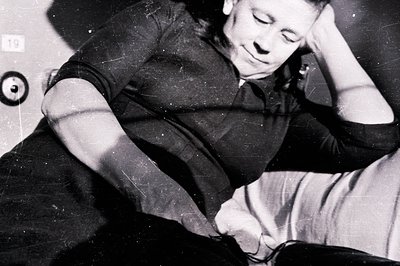 A young man rests, head in hands, propped against what appears to be a cushioned wall. Close-up shows strong highlights & sha...