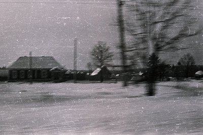 A snow-covered landscape features a low-slung building with a hipped roof & chimney, likely industrial or agricultural. Spars...