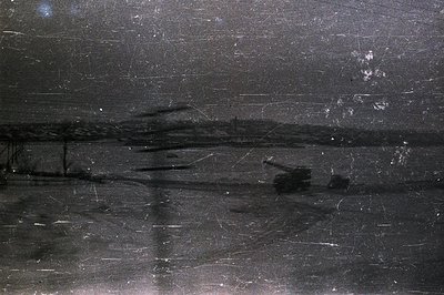 Monochromatic landscape featuring a body of water and distant treeline. Heavy grain & extensive scratches suggest age and pot...